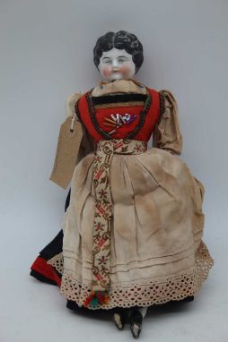 A continental porcelain headed doll, having fabric body and in orginal native dress, 30cm