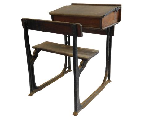 A 20thC oak school desk, with ink recess, a sloping hinged lid enclosing a vacant interior, with integrated bench, on a cast 