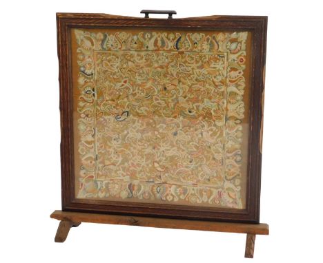 An early 20thC oak framed fire screen, inset with an embroidered panel decorated with leaves, scrolls, etc., 80cm high, 76cm 
