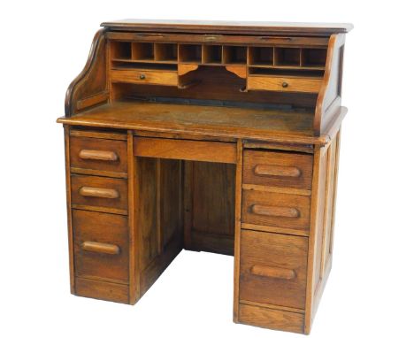 A 1920s oak roll top desk, the tambour front enclosing an arrangement of drawers, above three graduated drawers to each pedes