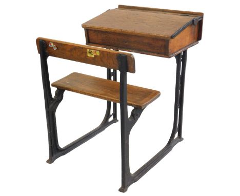 A 20thC oak school desk, with ink recess, a sloping hinged lid enclosing a vacant interior, with integrated bench, on a cast 