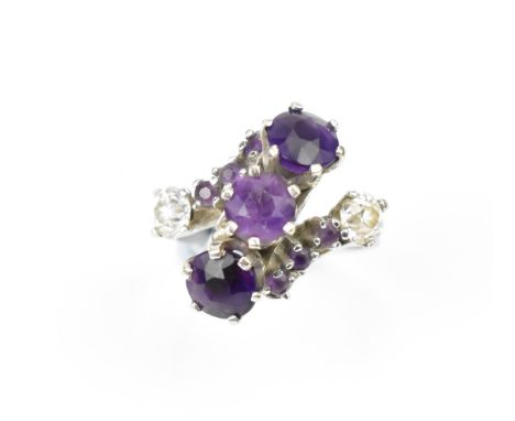 A white metal, diamond and amethyst dress ring, set with three central round cut amethyst flanked by three smaller ones eithe
