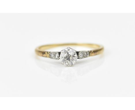 An Edwardian yellow metal and diamond solitaire ring, the central old cut stone flanked with two diamond accents either side,