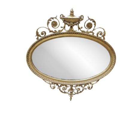 A late 19th Century attractive oval giltwood Mirror, decorated in the Adams taste with urn capital issuing floral scrolls, wi