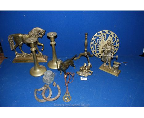 A box of brass including candlestick, horse doorstop, iron worker, horse shoes etc.