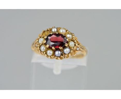 A 9CT GOLD GARNET AND PEARL CLUSTER RING, the central oval garnet within a split pearl surround (some replacement split pearl