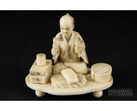 A small Japanese ivory okimono, c1910, carved in the form of a stone cutter seated with his tools of trade, on ivory base wit