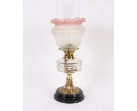 A Victorian brass column table oil lamp, having clear glass font and pink tinted shade, 54cm high overall