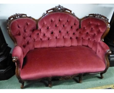 A VICTORIAN MAHOGANY BUTTON BACKED THREE SEAT SETTEE, THE TOP RAIL WITH THREE ROUND ARCHES CARVED WITH FRUITING FOLIAGE, THE 