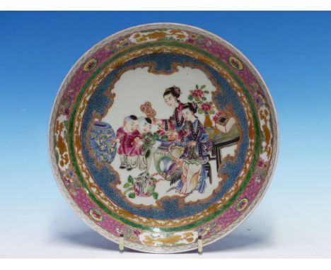 A CHINESE STYLE RUBY BACKED DISH PAINTED WITH TWO LADIES AND TWO CHILDREN WATCHING A CAT IN AN INTERIOR. Dia. 20.5cms.