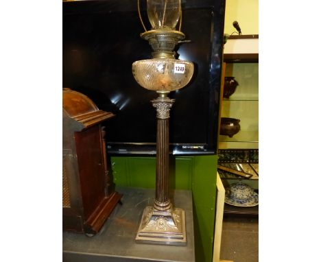 AN OIL LAMP WITH ENGRAVED AND CUT GLASS RECEIVER RAISED ON A SILVER PLATED CORINTHIAN COLUMN ON SWAG AND OVAL PATERAE DECORAT