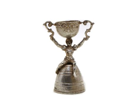 A Continental sterling silver wager cup,modelled as a figure seated upon an upturned barrel, holding aloft a rotating cup, im
