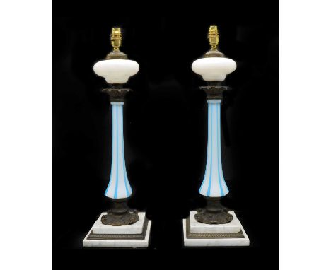 A pair of opaline glass table lamps,early 20th century, with gilt metal capital and blue line detail on stepped marble bases,