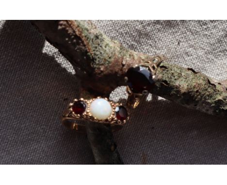 A 9ct gold opal and garnet ring, set with a central circular cabochon opal flanked by garnets to a 9ct gold setting and shank