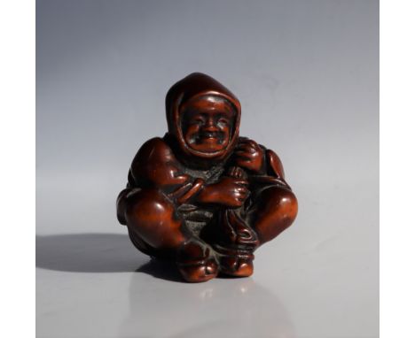 A 19th century Japanese carved wooden netsuke depicting a seated figure with a bag of spirits over its shoulders, 40mm high