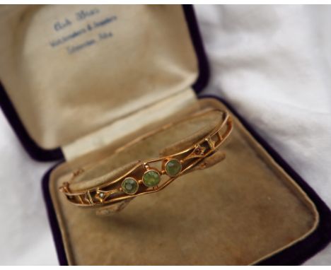 A 14ct yellow gold hinged bangle set with three round cut peridot and a seed pearl, approximately 8 grams 