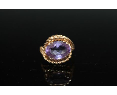 AN UNUSUAL HALLMARKED 9 CT GOLD AMETHYST RING, the gold being fashioned in a rope twist style, the oval amethyst measures app