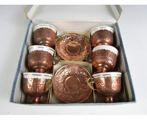 A 1930s boxed set of six copper and brass tea cups and saucers, with porcelain bowls, each element being chased and punched i