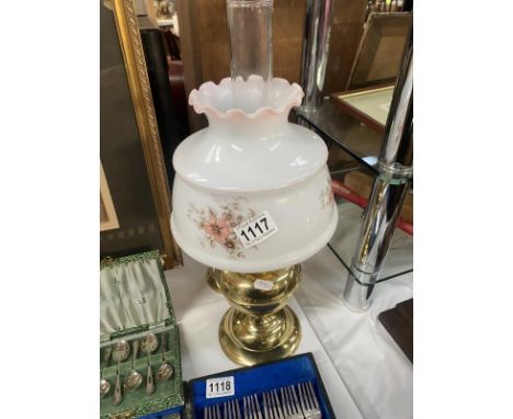 A brass oil lamp on reedes column with a floral glass shade