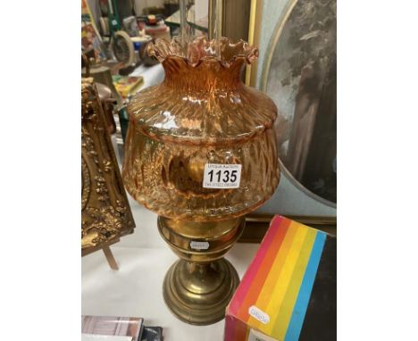 A brass oil lamp with amber coloured glass shade