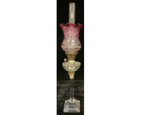 A late 19th century oil lamp, clear glass columnar stem, stepped square base, brass Corinthian capital, clear glass reservoir