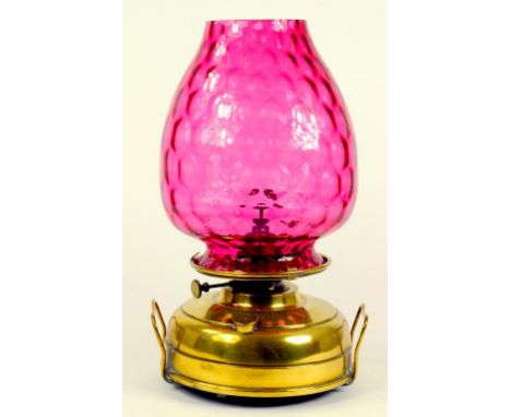 A BRASS OIL LAMP WITH DIMPLED CRANBERRY GLASS LAMPSHADE