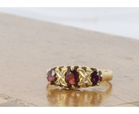 A garnet and diamond 18ct gold three stone ring, three oval garnets with pairs of small diamonds, ring size P, 2.4g 