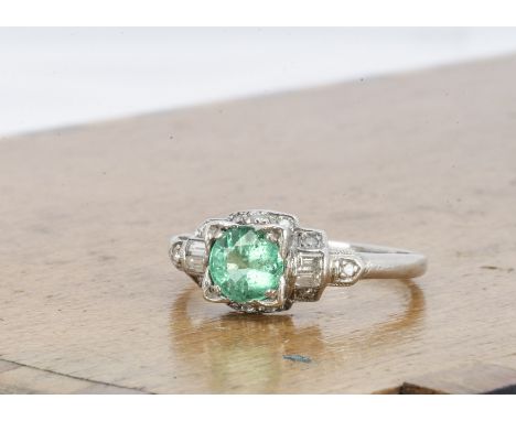 An Art Deco style emerald and diamond platinum dress ring, the round cut emerald with stepped shoulders surrounded by baguett