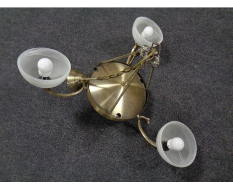A contemporary brass hanging ceiling light with three opaque glass shades 