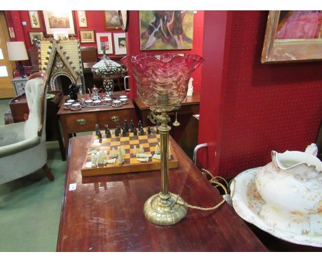 A Victorian brass oil lamp with cranberry tinted shade, converted to electric, 44cm tall
