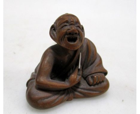 A 19th century wooden netsuke of a seated man holding an ivory stylus to his left shoulder as he gives a shout, signed Masaya