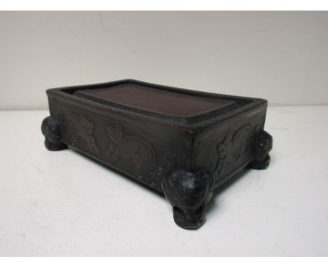 A blackened red ware inkstone, the rectangular top with raised centre flanked by a trough and S-scrolled rim, the sides with 