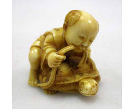 Masaharu', a late 19th century ivory netsuke carved as a child riding a minogame, a rope running from the child's mouth and r