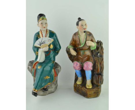 TWO ORIENTAL CERAMIC FIGURES, polychrome decorated, one a seated figure with a fan, the other seated beside bound sticks, bot