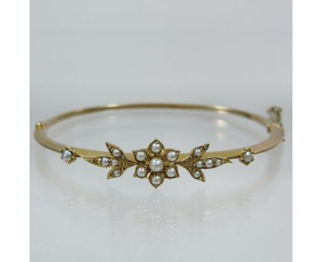 An early 20th century unmarked seed pearl bangle, of hinged design, with floral set split seed pearls, and safety chain 
