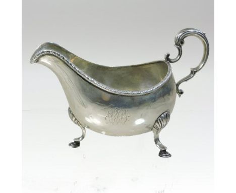 A George III Irish silver cream jug, of helmet shape, with a gadrooned rim, a scrolled handle, and monogram, on shell mounted