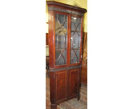 An Edwardian mahogany two sectional freestanding corner cupboard, the lower section enclosed by a pair of fielded panel doors