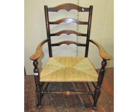 A beechwood ladder back elbow chair, with rush seat, raised on pad feet with turned rails 