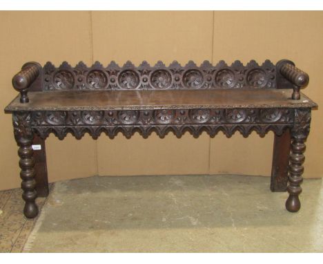 A late Victorian oak hall bench with repeating carved foliate detail, bobbin turnings and Gothic tracery detail, 122cm long x