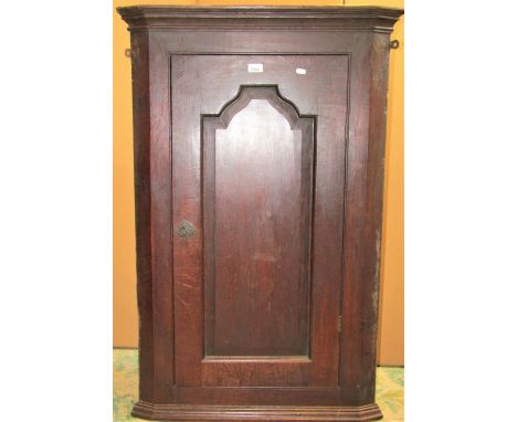 A Georgian oak hanging corner cupboard enclosed by a rectangular fielded arched moulded panelled door, the interior with arch