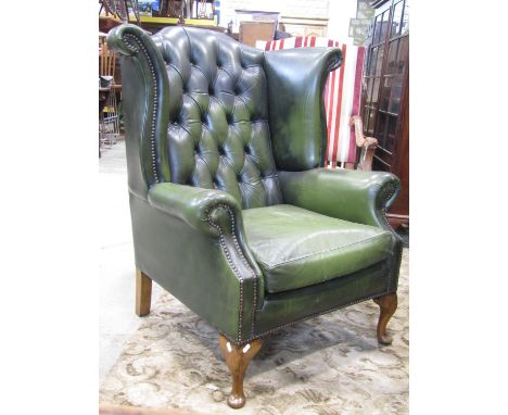 A reproduction Georgian style faux green leather upholstered wing armchair with button back, studded detail, loose seat cushi