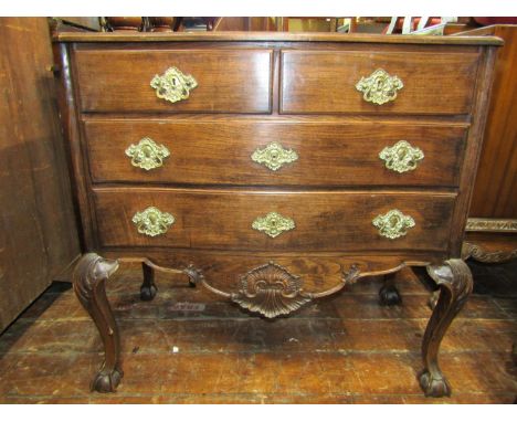An antique oak continental commode of shallow serpentine form, enclosing two long and two short drawers over a carved and sha