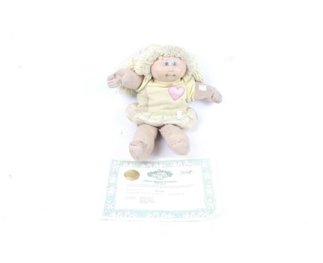 A Cabbage Patch doll. With blonde hair wearing a yellow dress, complete with card and certificate