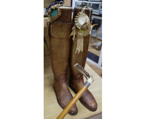 A pair of vintage riding boots with trees and a silver-collared cane riding stick