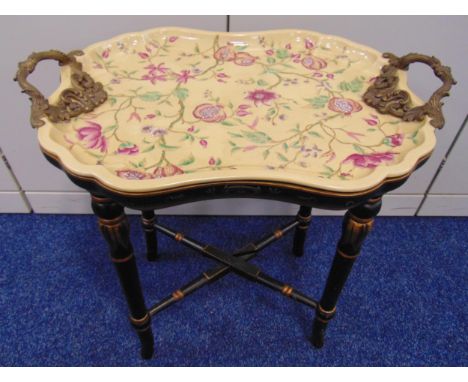 A continental shaped oval ceramic tea tray decorated with flowers and leaves and with pierced brass scroll side handles on gi