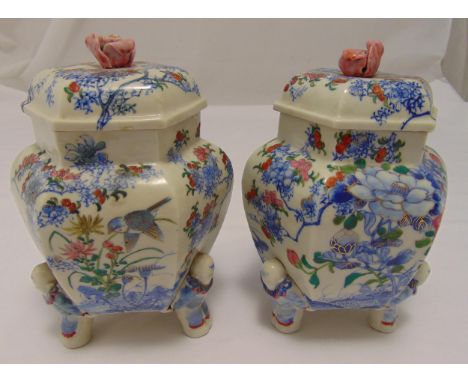 A pair of Japanese ceramic storage jars decorated with birds, flowers and leaves on four figural supports with domed pull off