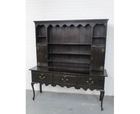 An oak dresser, the shelf plate back flanked by a pair of cupboard doors, over three drawers with brass handles, raised on ca