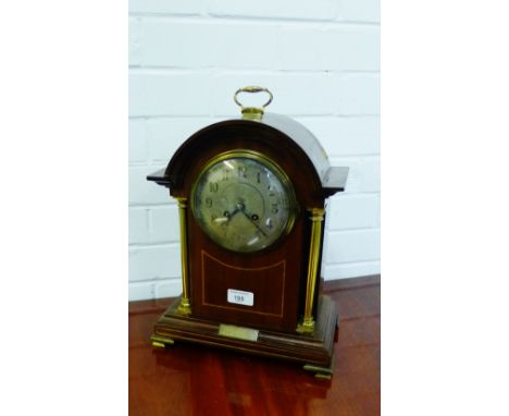 A mahogany and inlaid mantle clock, the arched top over a silver dial with Arabic numerals flanked by brass columns on a step