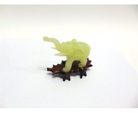A CARVED JADE FIGURE OF AN ELEPHANT,  standing with trunk raised, on hardwood stand 10cm high overall