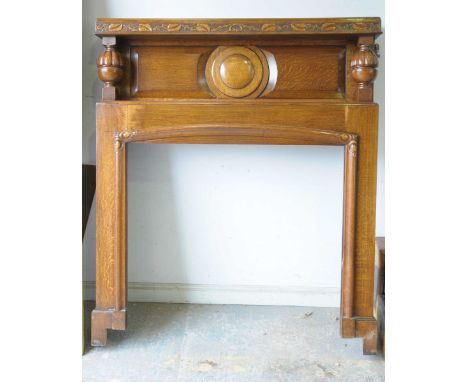 A mid 20th Century oak fire surround Having a vinery and leaf moulded frieze above a central roundel flanked by two semi-lobb